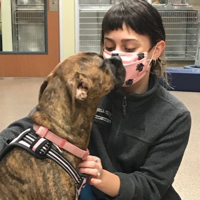 A woman in a face mask lovingly kisses her dog